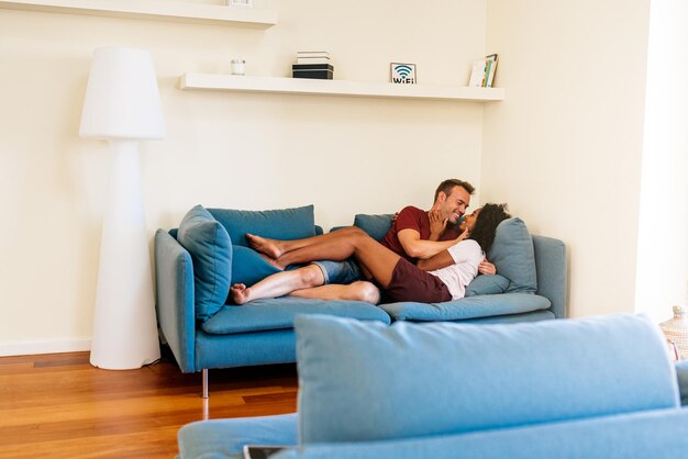 Idílica pareja multiétnica disfrutando mutuamente en el sofá en casa