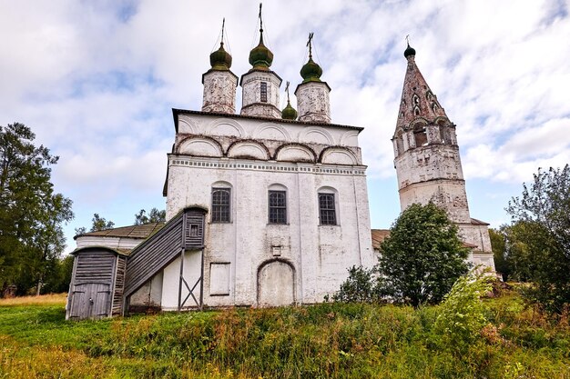 Iglesia ortodoxa vieja en el pueblo. Vista de verano con prado floral. Día soleado, cielo azul con nubes.