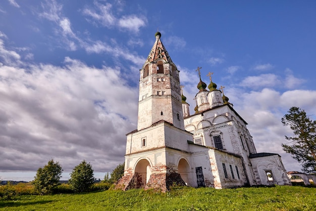 Iglesia ortodoxa vieja en el pueblo. Vista de verano con prado floral. Día soleado, cielo azul con nubes.