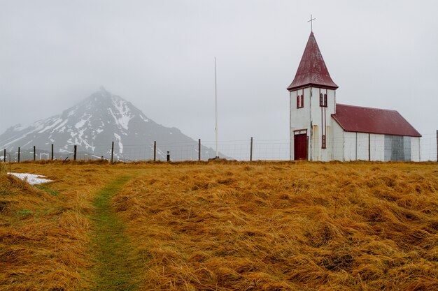 Iglesia con techo rojo en un campo rodeado de rocas bajo un cielo nublado en Islandia