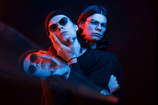 Ilusión de tres caras. Retrato de hermanos gemelos. Foto de estudio en estudio oscuro con luz de neón