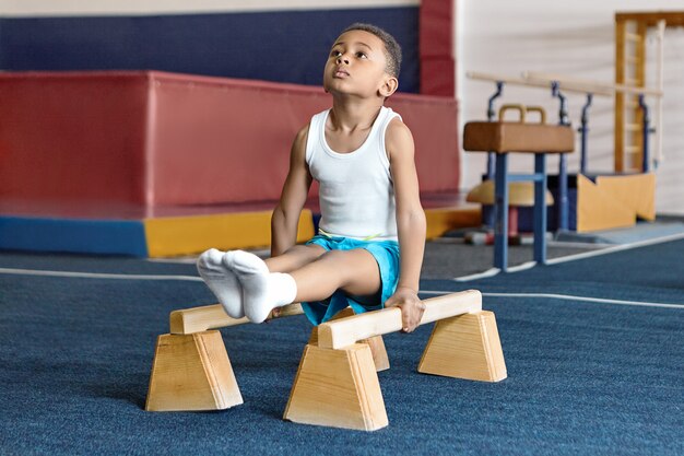 Imagen de la adorable pequeña gimnasta de piel oscura compitiendo en barras paralelas.