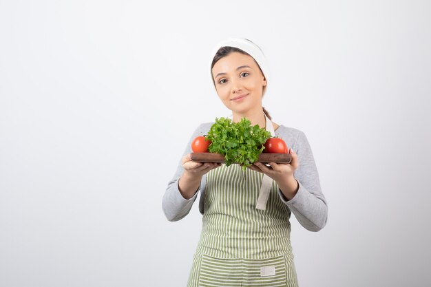 Imagen de una agradable mujer atractiva sosteniendo una tabla de madera con perejil y tomates