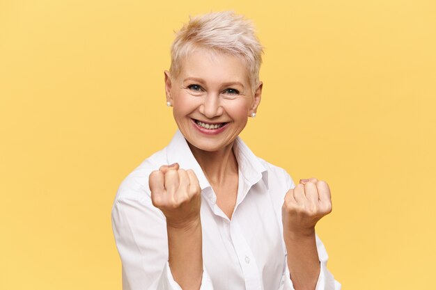 Imagen aislada de la empresaria europea independiente fuerte con el pelo corto teñido que expresa actitud positiva, sonriendo con confianza, apretando los puños. Mujeres, feminidad, poder, confianza y éxito