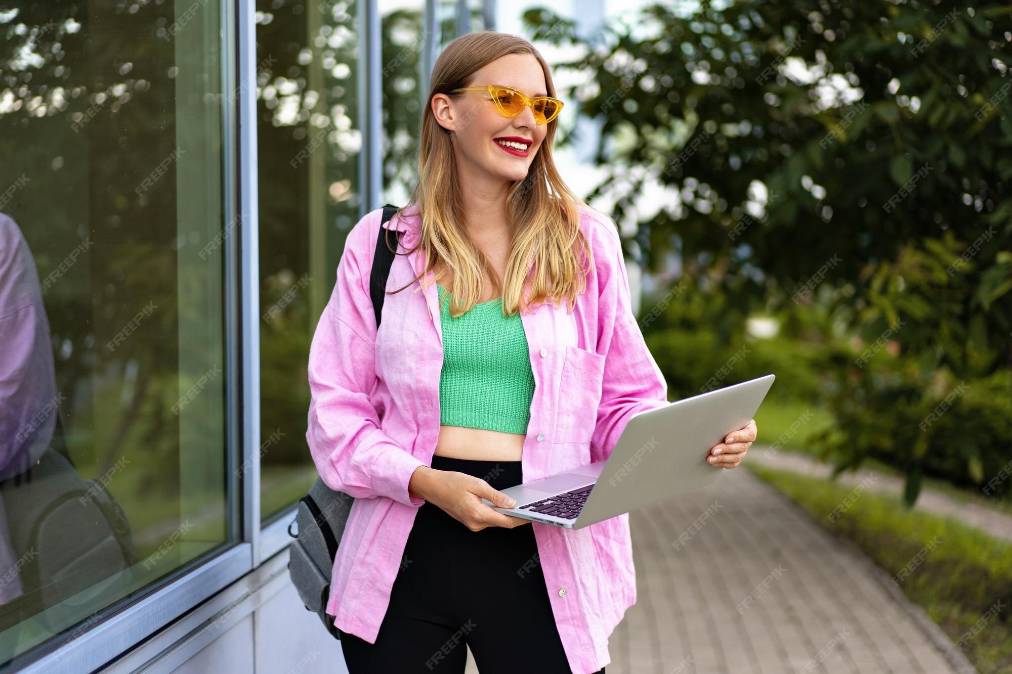 Imagen al aire libre de mujer blogger independiente rubia alegre y elegante, vestida con ropa casual brillante de moda, sosteniendo el bolso y la computadora portátil, lista para trabajar y