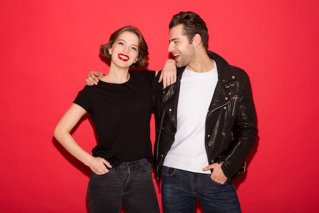 Foto gratuita imagen de la alegre pareja punk abrazando y posando juntos sobre la pared roja