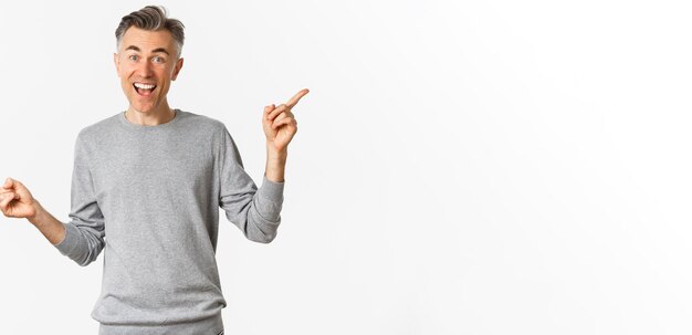 Imagen de un apuesto hombre de mediana edad con suéter gris que muestra dos variantes que señalan con el dedo hacia los lados de demostración
