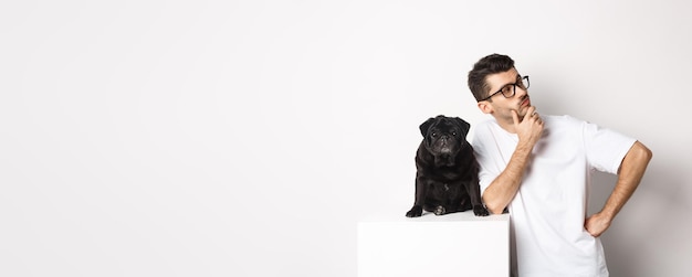 Imagen del apuesto joven dueño de una mascota de pie con su perro y mirando directamente al logo posando con pu