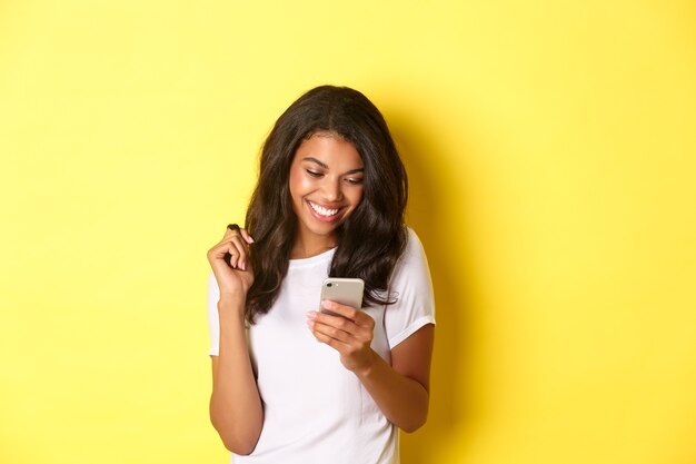 Imagen de atractiva chica afroamericana en mensajería de camiseta blanca en smartphone mirando móvil