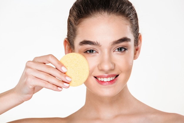 Imagen de la atractiva mujer morena con piel suave y sana aplicando maquillaje con esponja cosmética