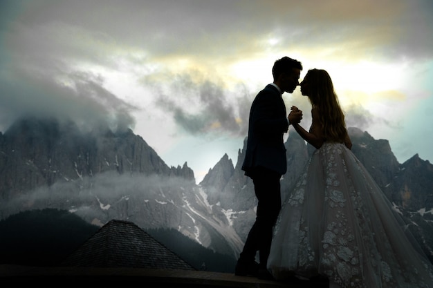 Imagen borrosa de besar a una pareja de novios de pie ante un magnífico paisaje de montaña