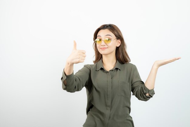 Imagen de una chica adorable con gafas dando pulgares hacia arriba sobre blanco. foto de alta calidad