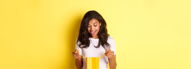 Foto gratuita imagen de una chica afroamericana feliz y sorprendida recibiendo un regalo mirando dentro de las compras mal con