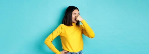 Foto gratuita imagen de una chica asiática con estilo que cierra la nariz y hace una mueca de aversión, algo huele mal de pie d