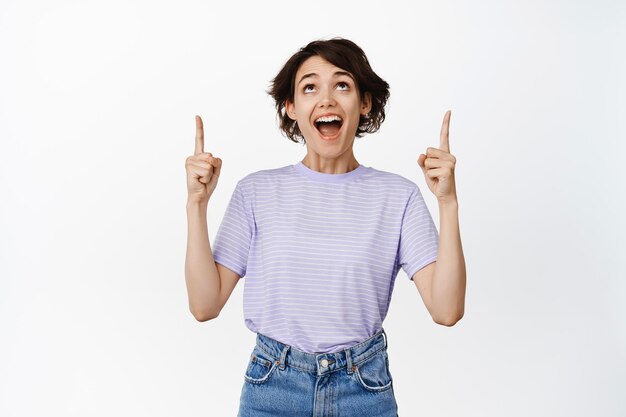 Imagen de una chica asombrada y súper feliz mirando con la cara fascinada y asombrada, señalando con el dedo el logotipo, promoción de venta, mostrando publicidad, fondo blanco.