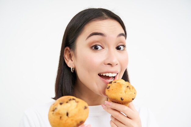 Imagen de una chica coreana feliz que ama los pasteles sonriendo y comiendo pastelitos aislados de fondo blanco