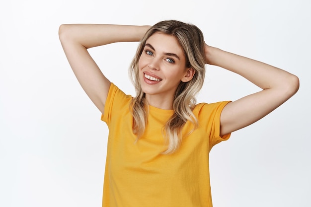 Imagen de una chica feliz y hermosa relajándose descansando con las manos detrás de la cabeza y sonriendo luciendo libre y descuidada de pie contra el fondo blanco