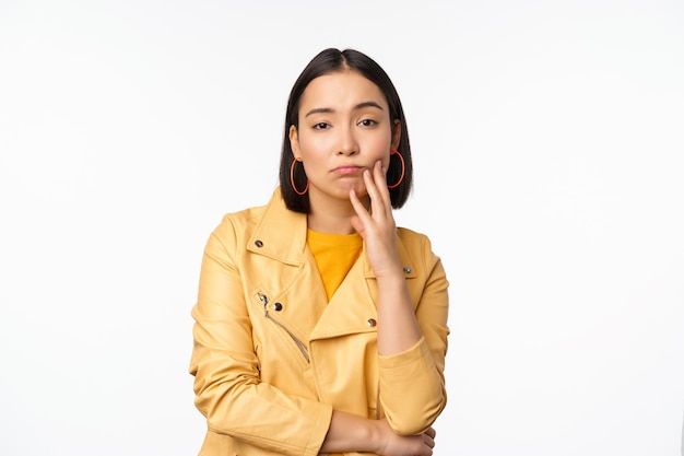 Imagen de una chica japonesa con estilo que mira con una expresión de cara cansada y molesta sin diversión de pie con ropa informal sobre fondo blanco