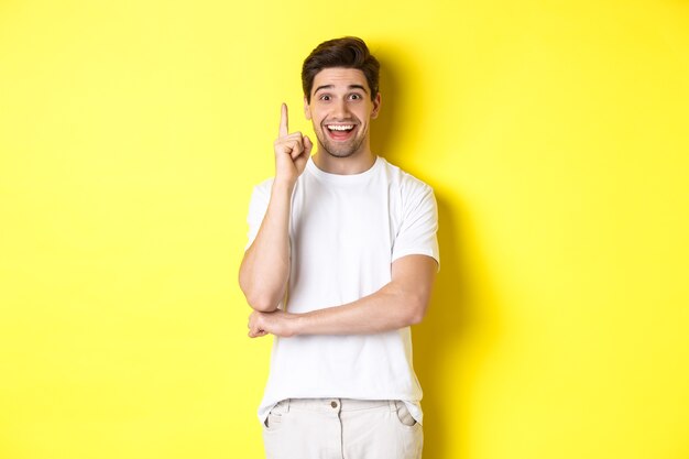 Imagen de un chico atractivo que tiene una idea, levantando el dedo y sugiriendo un plan, sonriendo emocionado, de pie sobre un fondo amarillo.