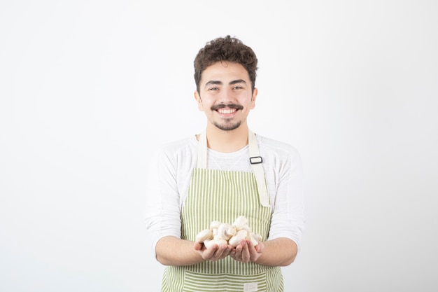 Imagen de cocinero masculino sosteniendo setas crudas con expresión feliz en blanco