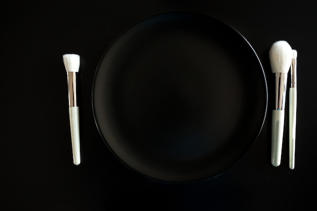 Imagen conceptual de pinceles de maquillaje junto al plato sobre fondo negro