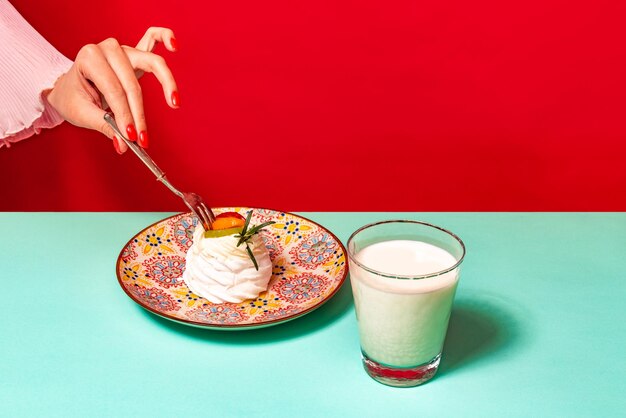 Imagen coorful de delicioso postre de merengue y vaso de leche aislado sobre fondo verde y rojo