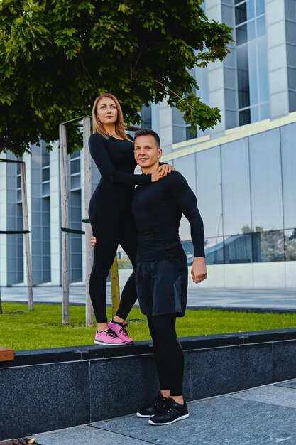 La imagen de cuerpo completo de la pareja de fitness atlético está posando sobre el fondo del edificio moderno.