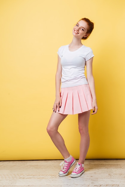Imagen de cuerpo entero de la atractiva chica de jengibre con camiseta y falda mirando