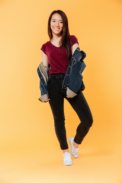 Imagen de cuerpo entero de feliz mujer asiática en chaqueta de mezclilla posando