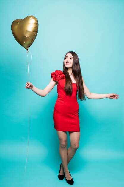 Imagen de cuerpo entero de hermosa mujer en elegante traje rojo posando con globo en forma de corazón, aislado