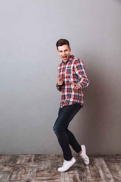 Foto gratuita imagen de cuerpo entero del hombre satisfecho en camisa y jeans apuntando y mirando