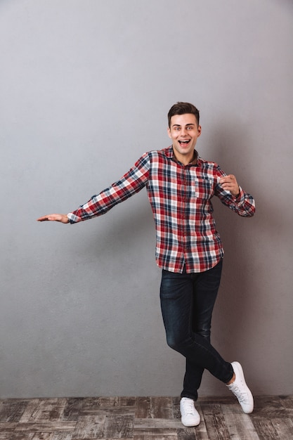 Imagen de cuerpo entero del hombre sonriente en camisa y jeans tocando copyspace y señalando