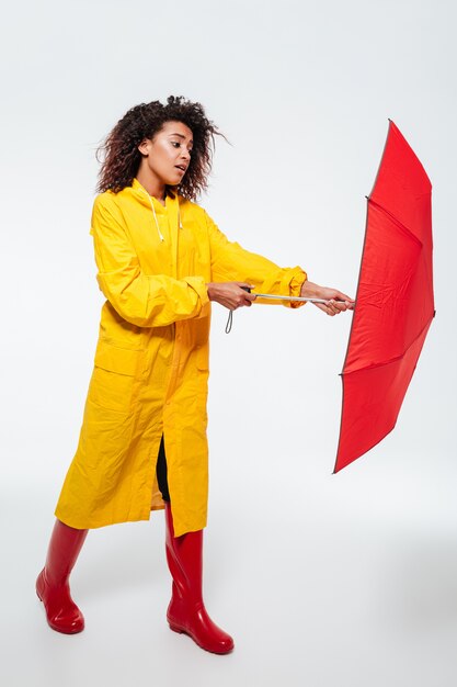 Imagen de cuerpo entero de mujer africana confundida en impermeable abrir paraguas