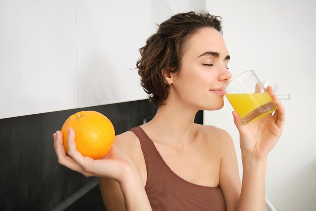 Imagen de una deportista de fitness sosteniendo un vaso de jugo y una naranja sonriendo bebiendo una bebida de vitaminas