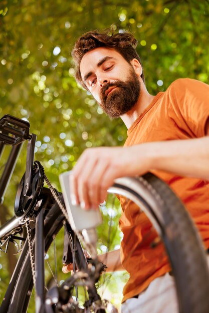 Imagen detallada de la cadena de bicicletas moderna que se lubrica meticulosamente con grasa para un ocio seguro al aire libre. La imagen muestra el anillo del freno de disco de la bicicleta siendo engrasado por un ciclista masculino como mantenimiento de verano