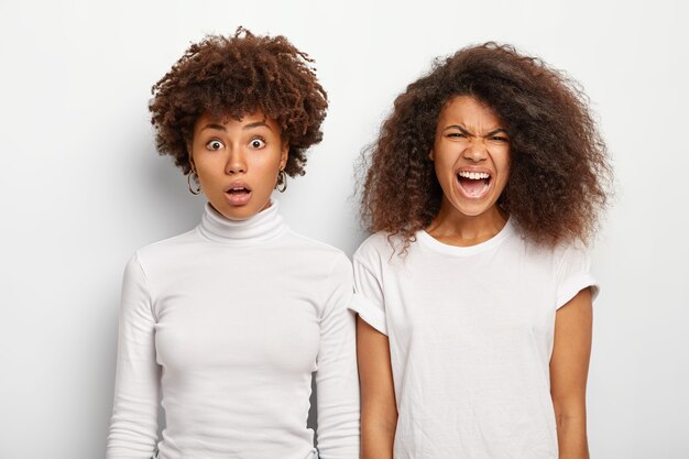 Imagen de dos hermanas afroamericanas reaccionan ante algo malo, una mira con estupor