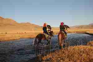 Foto gratuita imagen de dos jinetes en un río rodeado por un valle desierto con colinas
