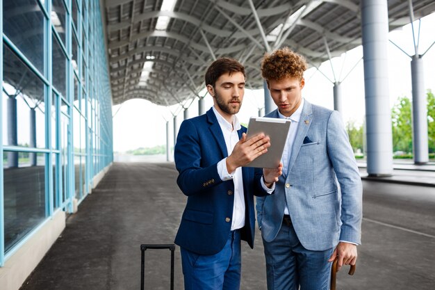 Imagen de dos jóvenes empresarios hablando en la estación y sosteniendo la tableta