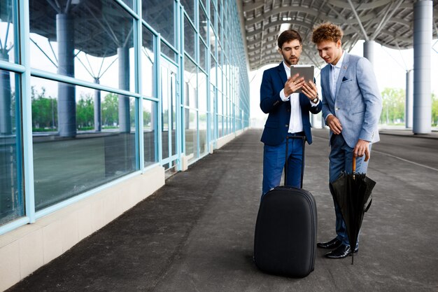 Imagen de dos jóvenes empresarios hablando en la estación y sosteniendo la tableta