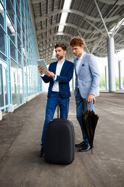 Imagen de dos jóvenes empresarios hablando por terminal y sosteniendo tableta