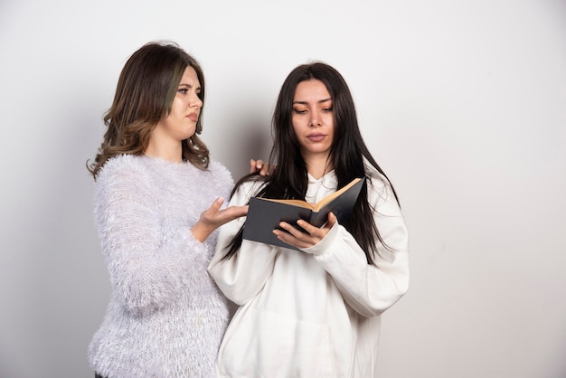 Imagen de dos mejores amigos parados juntos y mirando un libro en la pared blanca.