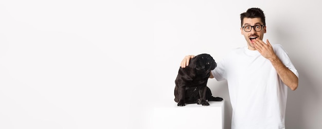 Foto gratuita imagen del dueño del perro sorprendido y feliz acariciando a su perro y mirando a la cámara con regocijo de pie con