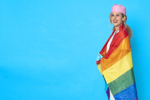 Imagen de una enfermera sonriente con una bandera LGBT contra un fondo azul.