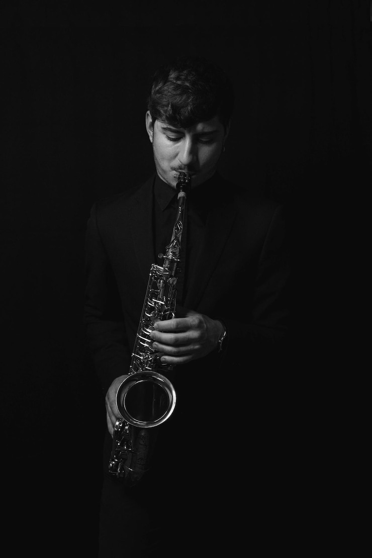 Foto gratuito imagen en escala de grises de un tipo genial y guapo tocando su saxofón aislado en un fondo oscuro