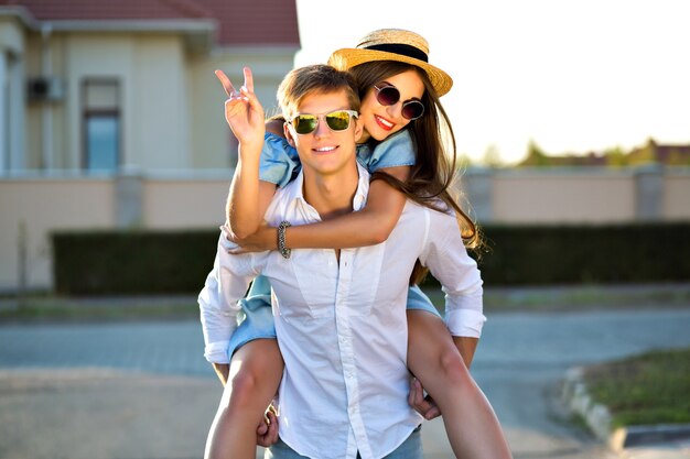 Imagen de estilo de vida al aire libre de una pareja feliz enamorada divirtiéndose y volviéndose locos juntos, abrazos y besos, cita romántica, luz del sol por la noche, calle, viajes, chicos elegantes y elegantes, amantes hermosos.