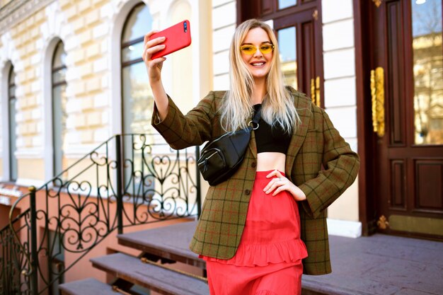Imagen de estilo de vida de rubia elegante bastante elegante haciendo selfie en la calle,