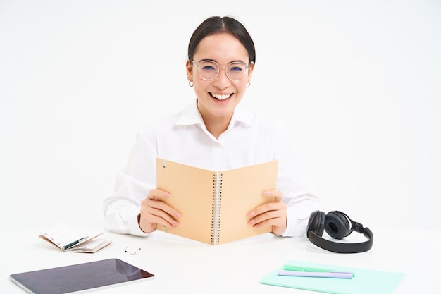 Foto gratuita imagen de una estudiante trabajadora asiática con anteojos estudiando sosteniendo un cuaderno trabajando en el proyecto iso