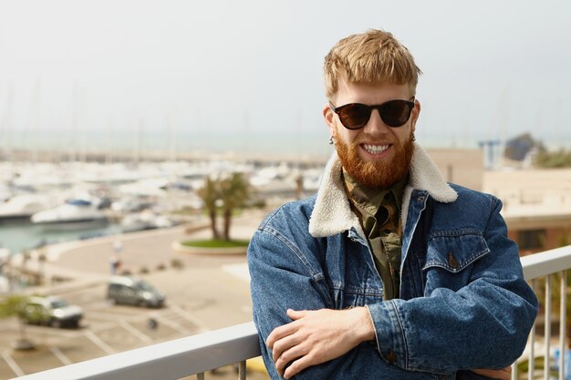 Imagen exterior de alegre moda joven macho europeo con larga barba pelirroja