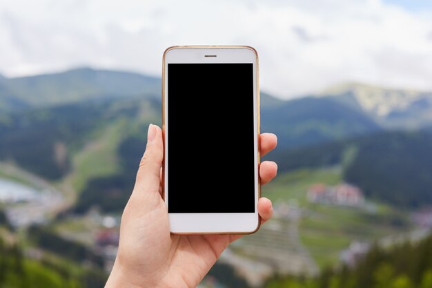 Imagen exterior de una mano sosteniendo y mostrando un teléfono inteligente blanco con una pantalla de escritorio negra en blanco