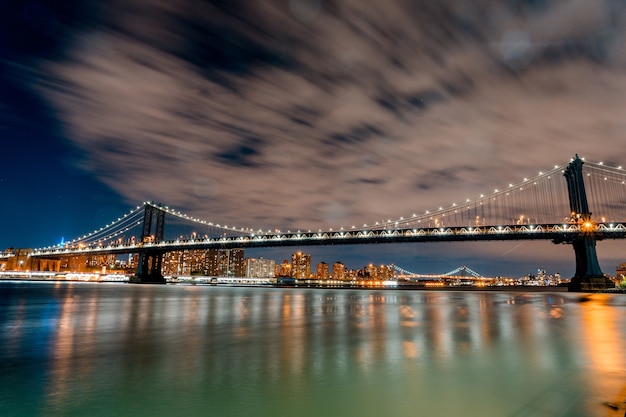 Imagen fascinante del Puente de Brooklyn y luces que se reflejan en el agua por la noche en los EE. UU.